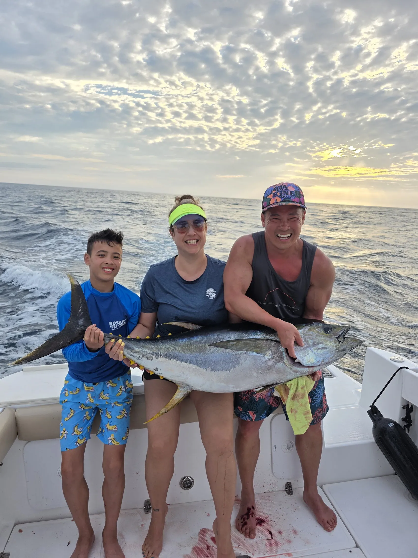 Three guests with a yellowfin tuna on the deck at sunset